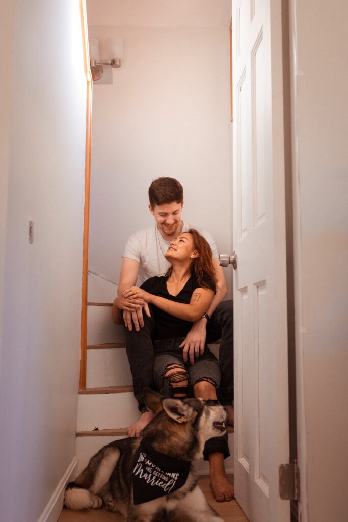 man and woman smile at each other during engagement pictures at home