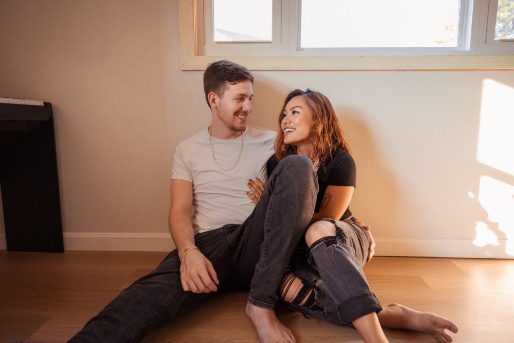 man and woman sitting on the floor smiling during at home engagement photos