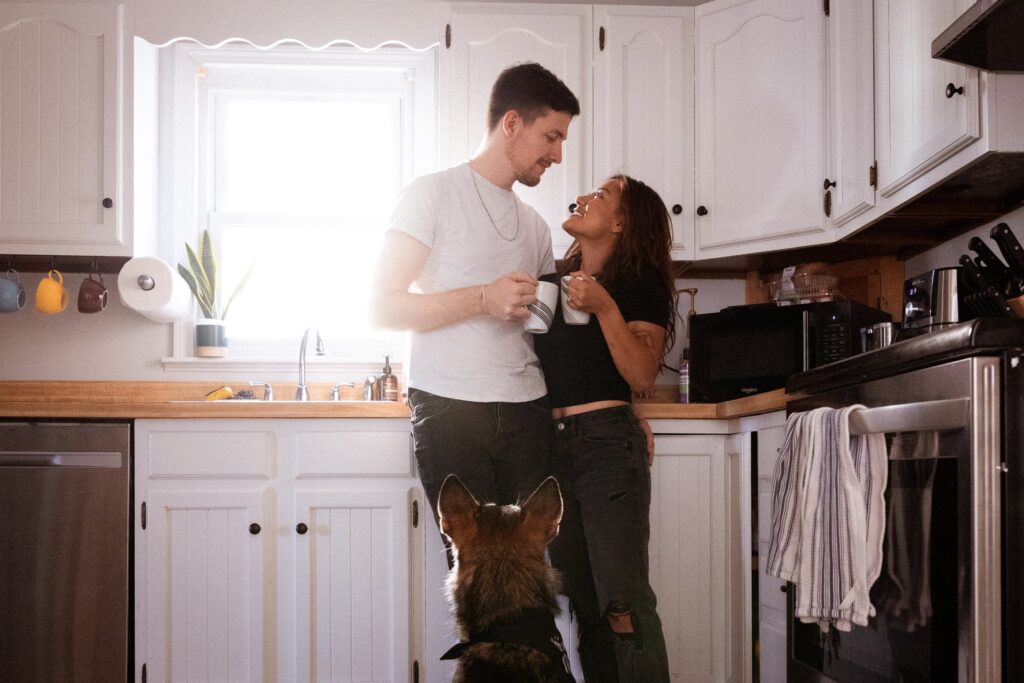 man and woman drink coffee as their dog looks on during engagement photos at home