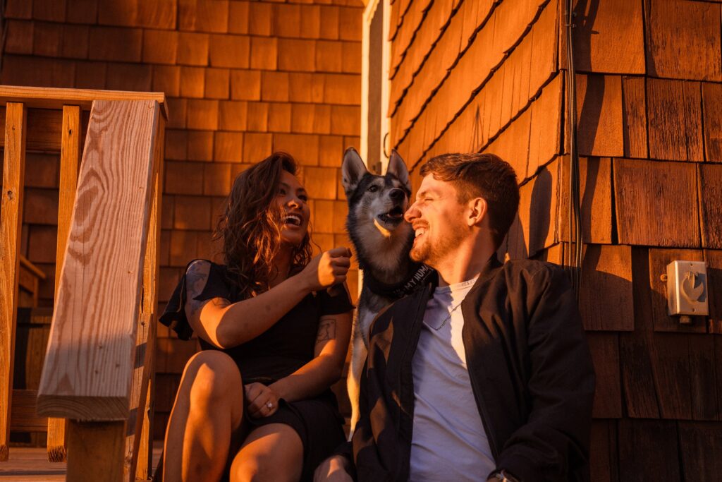 couple laughs with dog during couples photos in their backyard