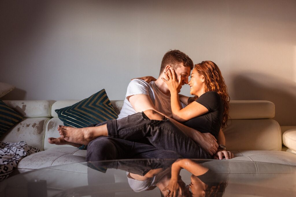 couple cuddles on couch during casual engagement photos at home