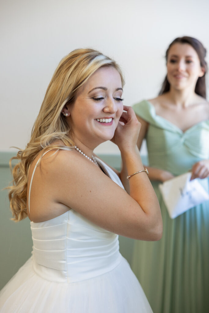 Bride puts on her earrings with her maid of honor in the background