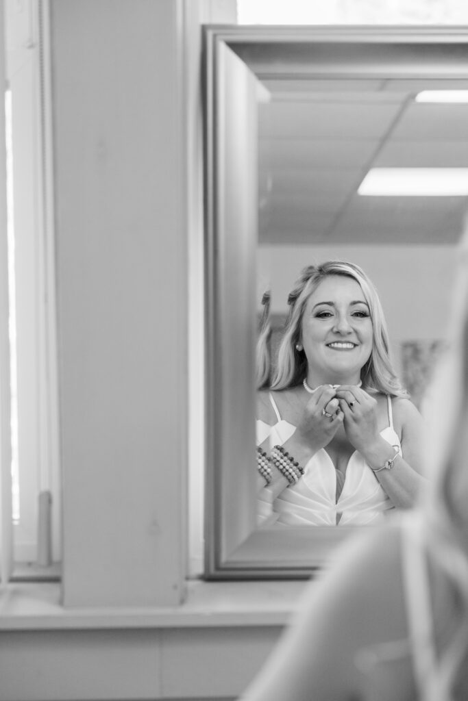Bride puts on her pearl necklace in black and white