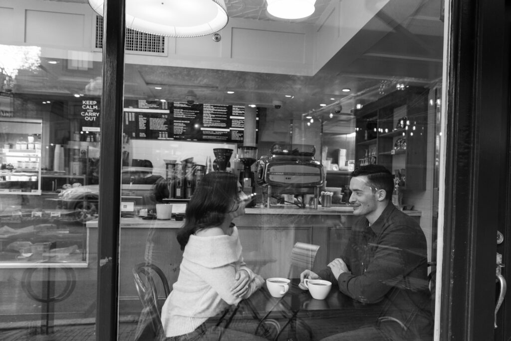 man and woman smile while drinking coffee during engagement photos in Boston