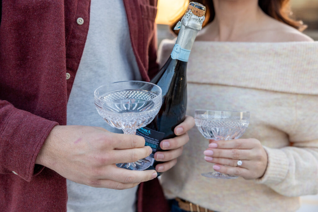 man and woman hold champagne glasses during engagement photos