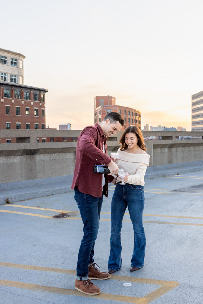 couple pops bottle of champagne during engagement photoshoot