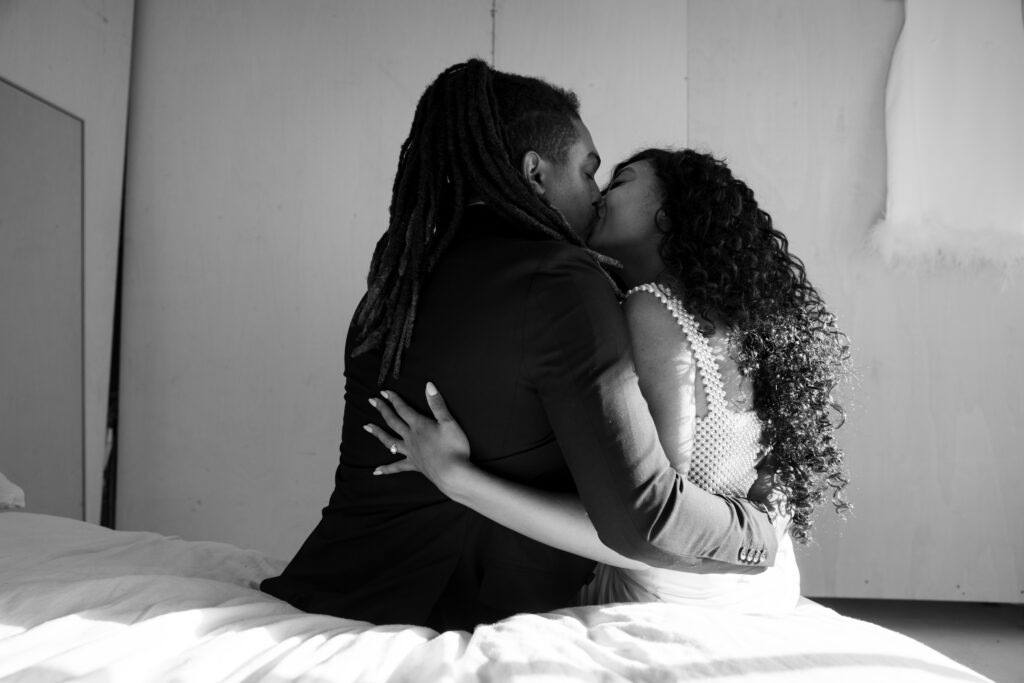 Bride and groom kiss sitting on the bed in black and white.