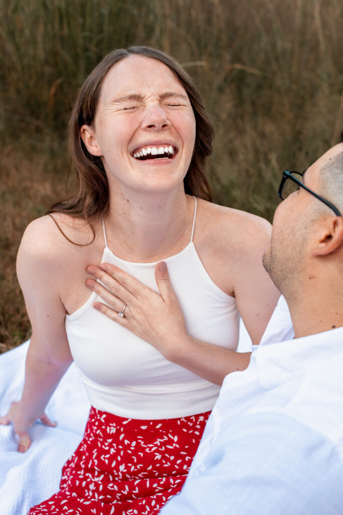 Engaged couple session at the Arnold Arboretum. Diverse Couple, engaged mixed couple black and white sitting down in front of a wheat field Candid moments woman is laughing. Detail shot of her engagement ring.