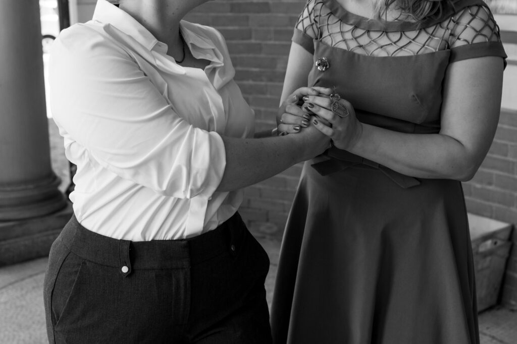 LGBTQIA+ couple elopes. Detail photo of their attire and them holding hands in Black and white