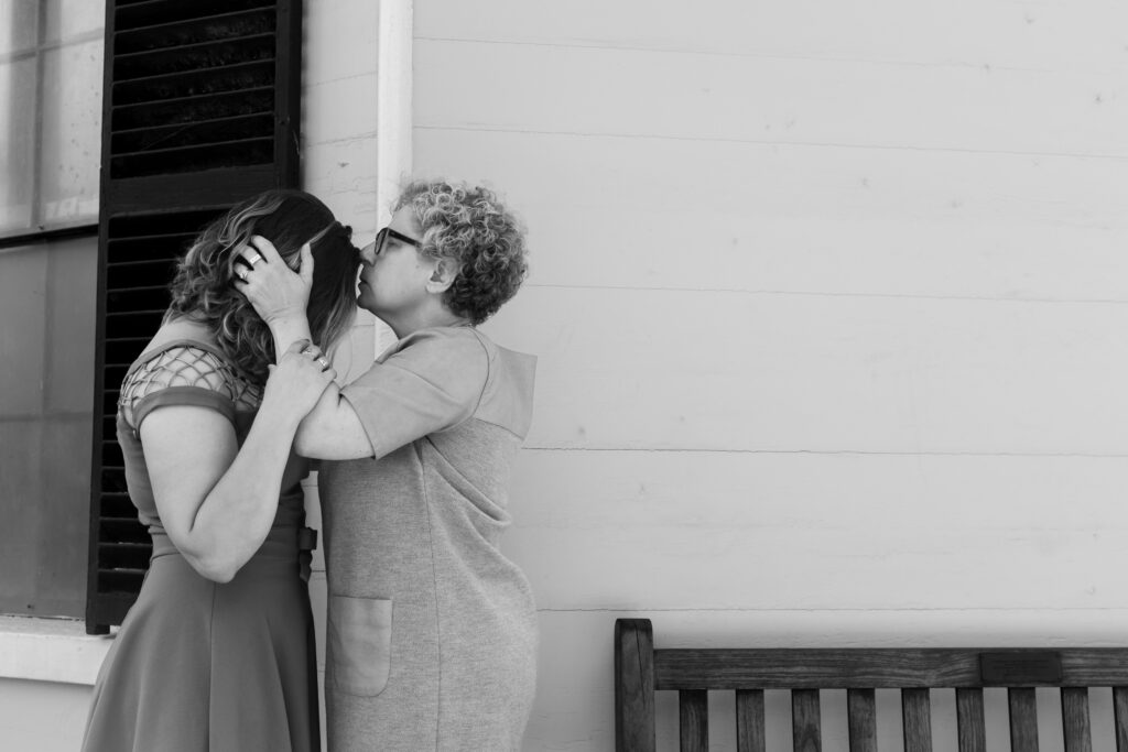 LGBTQIA+ couple elopes. Candid Wedding Family Portraits, Mother kisses daughter on her forehead in back and white