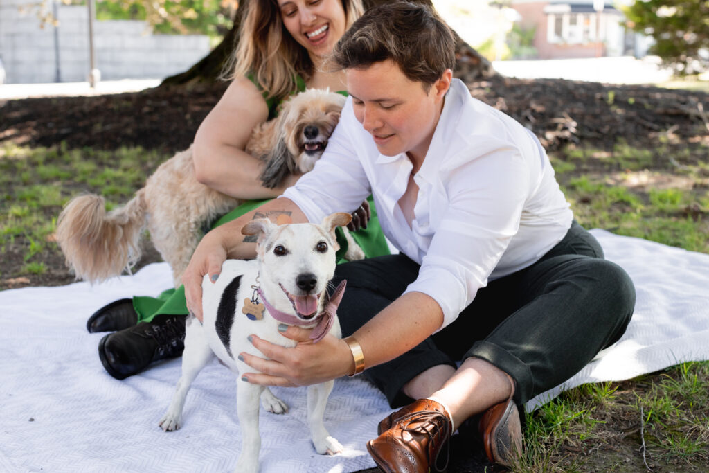 LGBTQIA+ couple elopes. Candid Wedding Portraits with their dogs sitting down on a picnic blanket