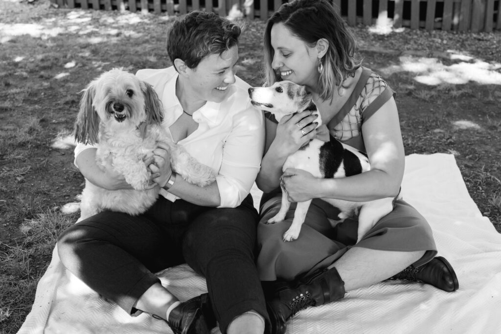 LGBTQIA+ couple elopes. Candid Wedding Portraits with their dogs sitting down on a picnic blanket in black and white