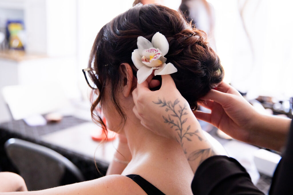 The bride getting her hair done and gets a orchid placed in as the flower detail
