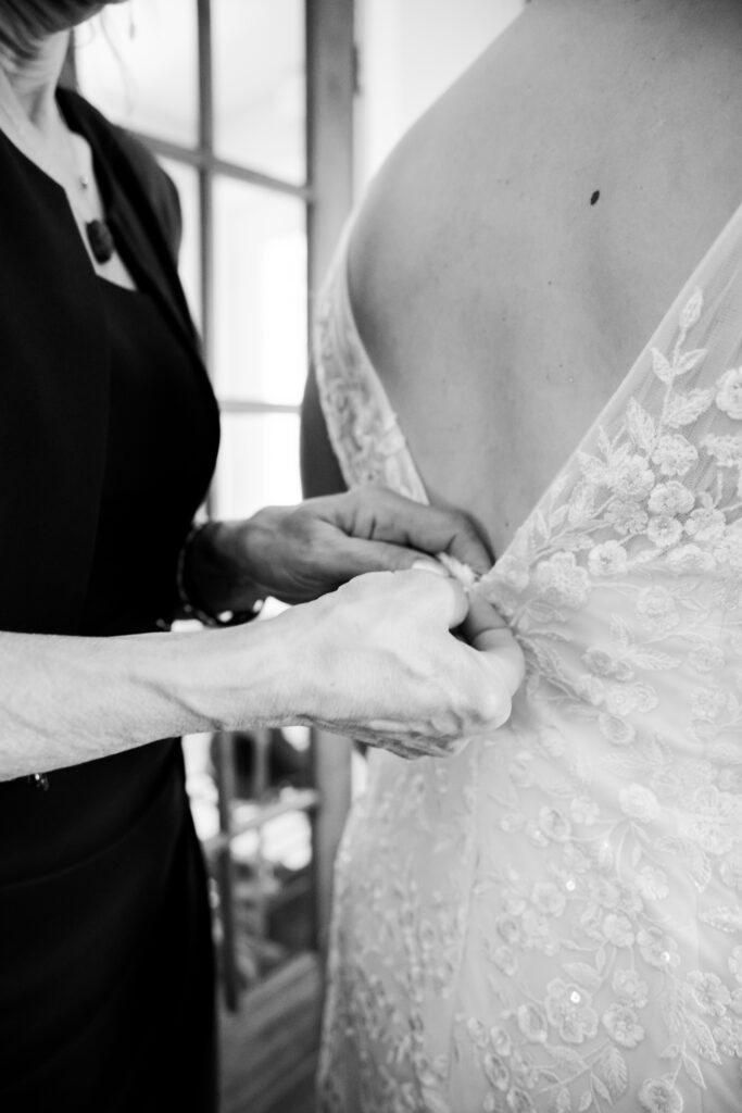 Bride’s mother helps her zip up her wedding dress in black and white