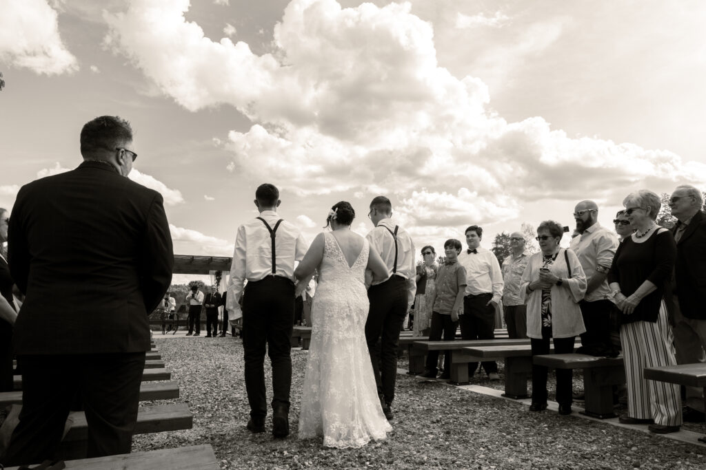 The bride is walked down the aisle by both of her kids at the wedding ceremony In black and white