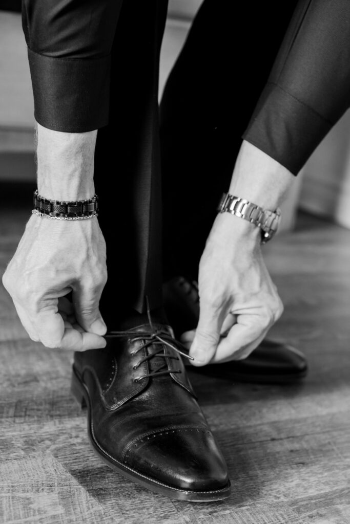 Groom ties his shoes before the wedding as he gets ready in black and white