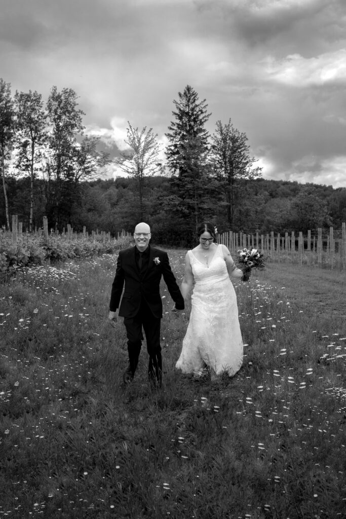 Bride and groom walking in a field of wildflowers at their summer vineyard wedding in black and white