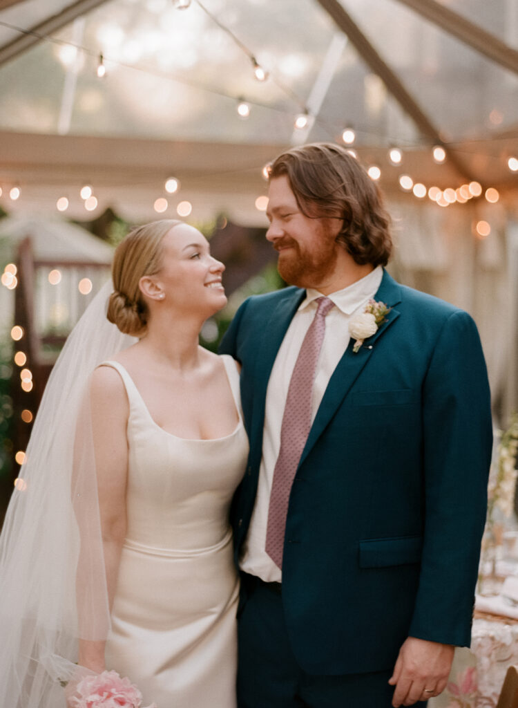 Bride and groom share a quiet moment under string lights at their backyard tent wedding, captured on medium format film by wedding film photographer