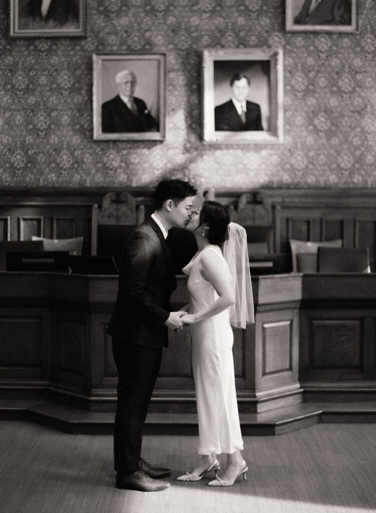 Anna and Huimin standing hand in hand inside Cambridge City Hall as they say “I do” on Valentine’s Day.