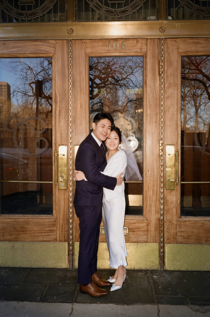Newlywed couple standing in front of dramatic vintage doors in Boston’s Theater District during their Cambridge City Hall elopement, captured on film by a Boston elopement photographer.