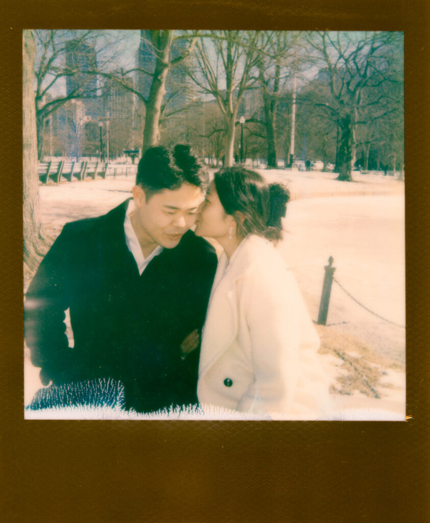 Couple laughing near frozen pond in Boston Public Garden during winter elopement on polaroid film.