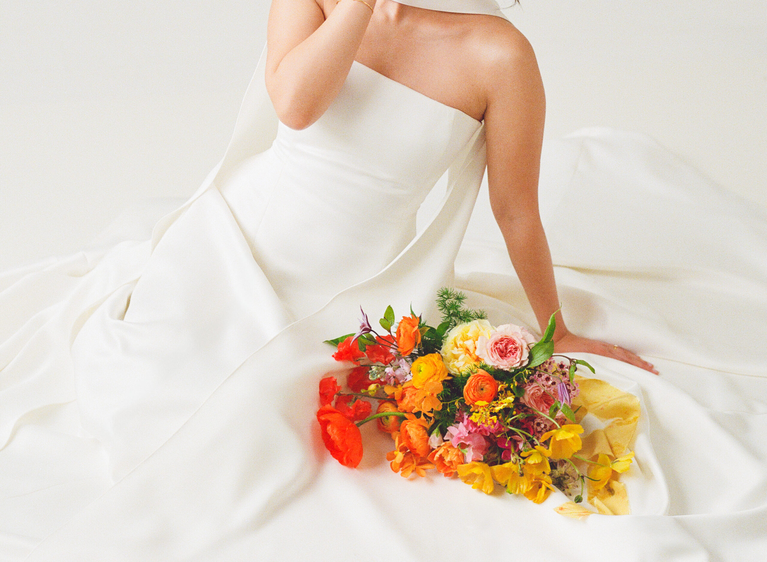 Close-up of a modern bride in a minimalist white wedding dress holding a vibrant spring bouquet with poppies, ranunculus, and garden roses. Captured on film by a film wedding photographer in New England for a colorful wedding editorial.