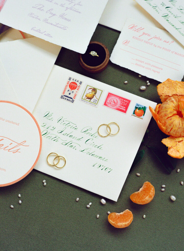 Modern citrus wedding invitation suite photographed on 35mm film. This flatlay features tangerine accents, vintage stamps, elegant calligraphy, and pearl details—perfect inspiration for couples planning a colorful spring wedding. Film wedding photographer in Boston