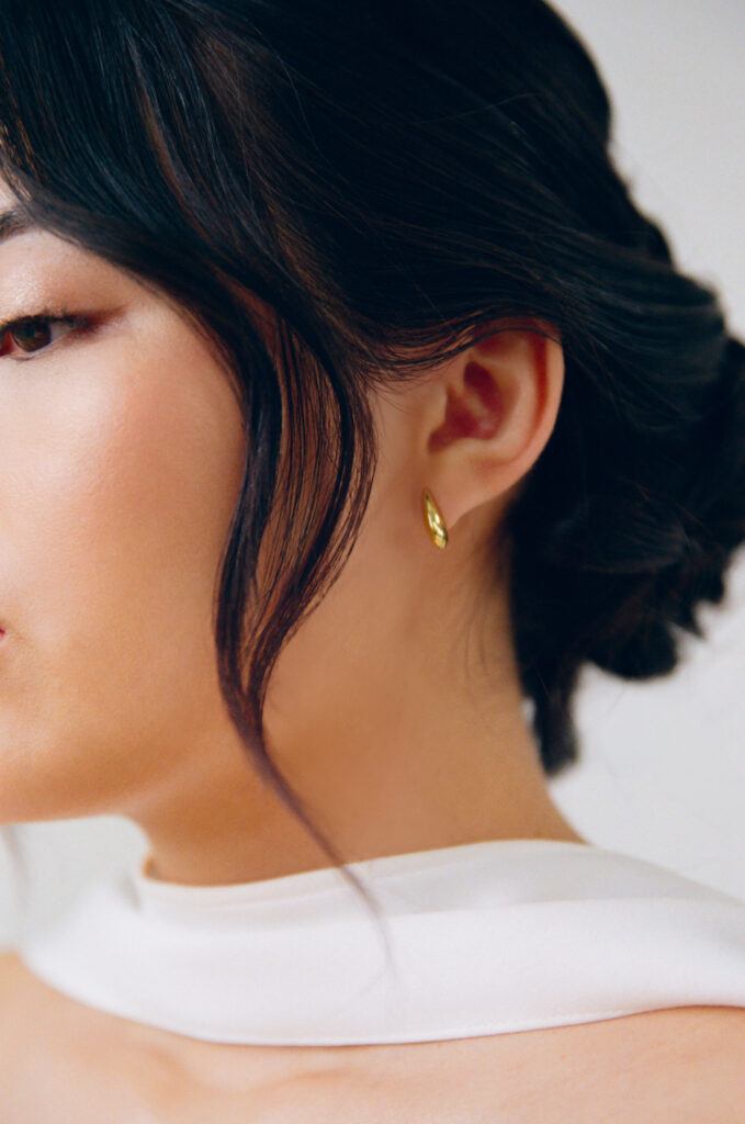 Detail shot of minimalist bridal beauty featuring gold wedding earrings, soft glam makeup, and an elegant bridal updo. Captured on film as part of a modern Boston wedding editorial with fashion-forward styling.