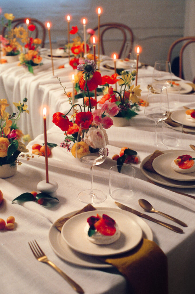 Warm candlelit wedding reception with citrus tones and spring florals. Vibrant wedding tablescape inspiration featuring blood orange pavlovas, silk napkins, and colorful flower arrangements. Captured on film by a New England-based film wedding photographer.