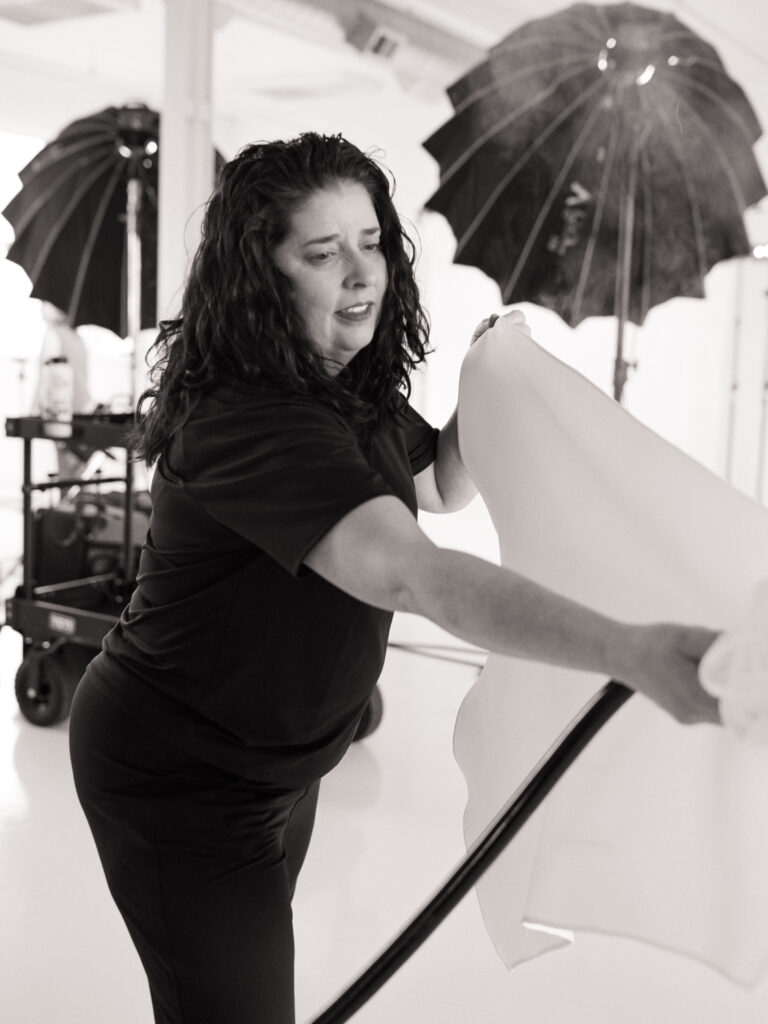 Black and white film photo of @christinecornellbridaldresser steaming a wedding dress on set for the Spring 2025 editorial.
