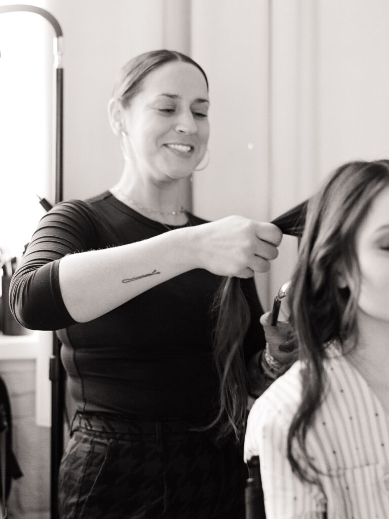 Black and white film photo of @naturallyawright curling a model’s hair on set for the Spring 2025 editorial.