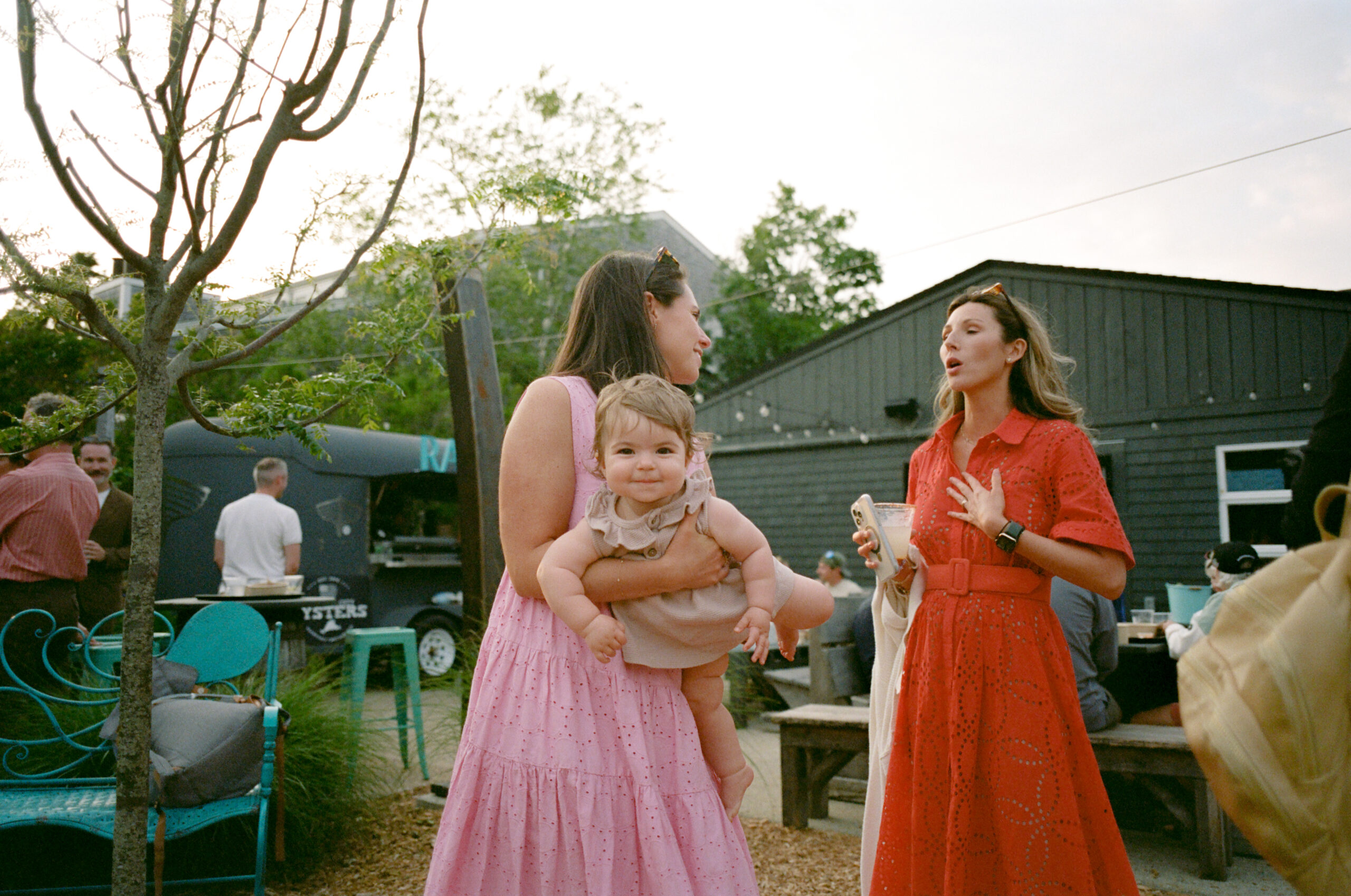 Guest holding her baby while mingling at Noman’s during a Martha’s Vineyard rehearsal dinner on film.
