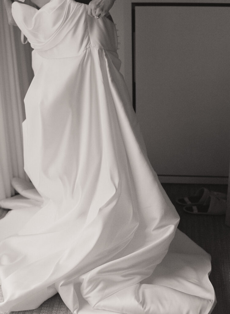 Black and white film photo of a bride in an elegant strapless wedding gown, the fabric cascading in soft folds as she prepares for her day on Martha’s Vineyard.