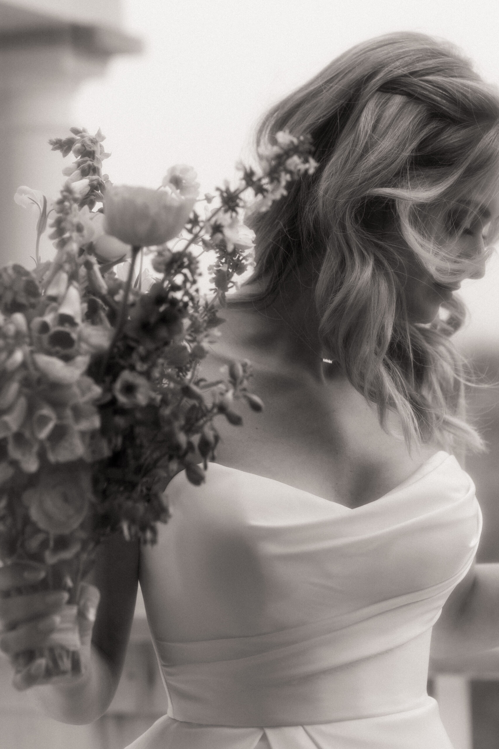 Soft black and white film portrait of a bride holding her bouquet, wind in her hair, capturing a dreamy and romantic detail before her Martha’s Vineyard wedding ceremony.