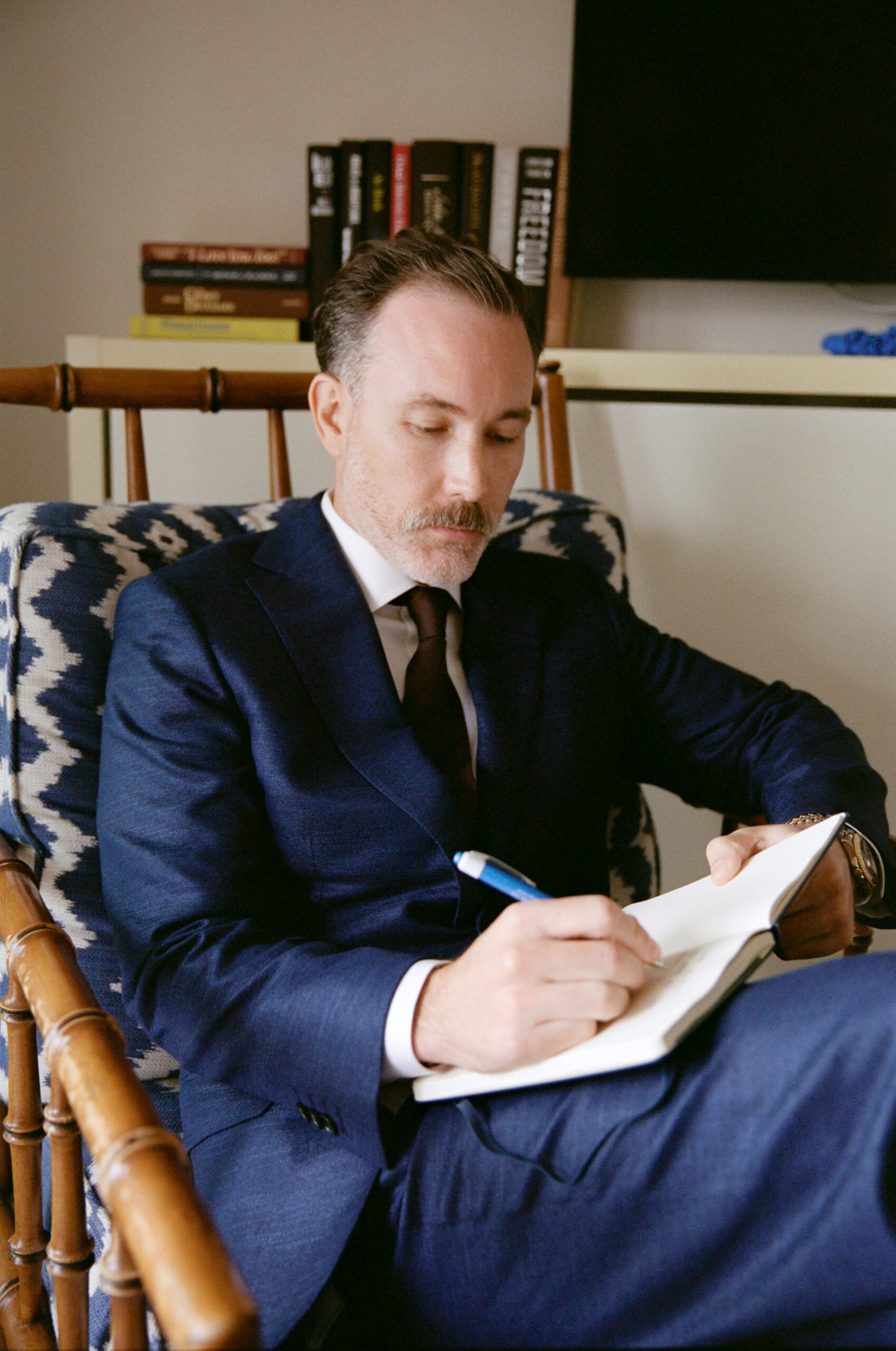 Color film photo of the groom in a navy suit, writing in a journal on the morning of the wedding.