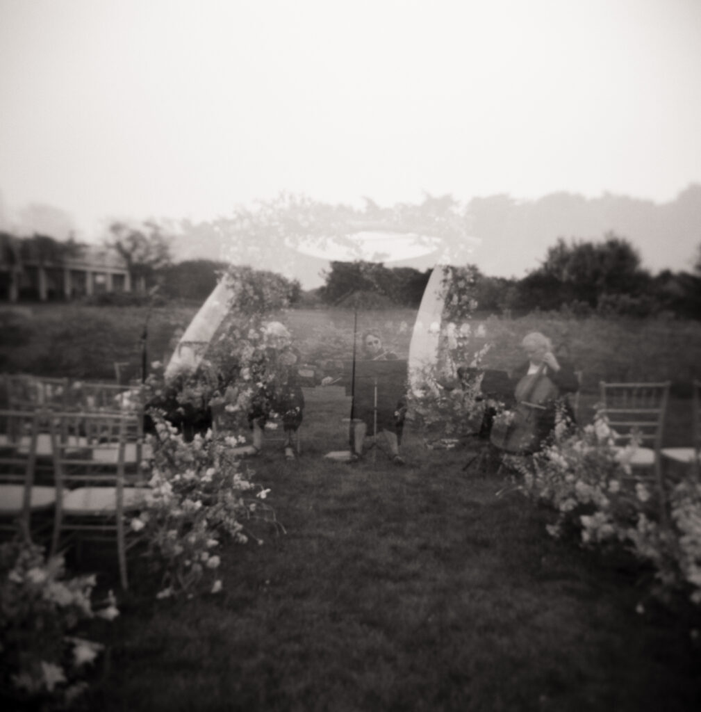 Double exposure film photo of floral wedding arch and string musicians setting up for an outdoor Martha’s Vineyard ceremony.