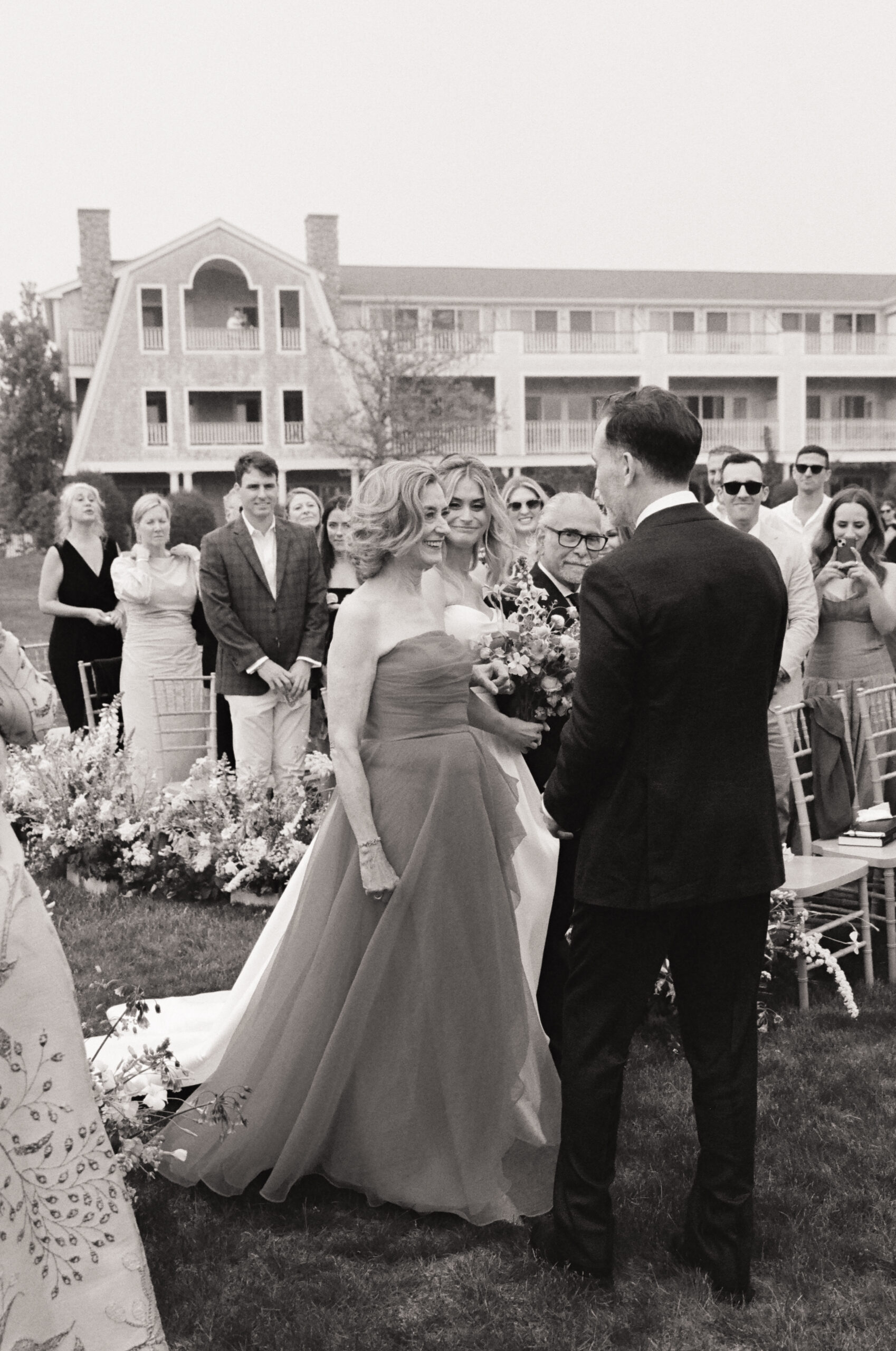 Bride walking down the aisle with family, emotional black and white film wedding photograph in New England.