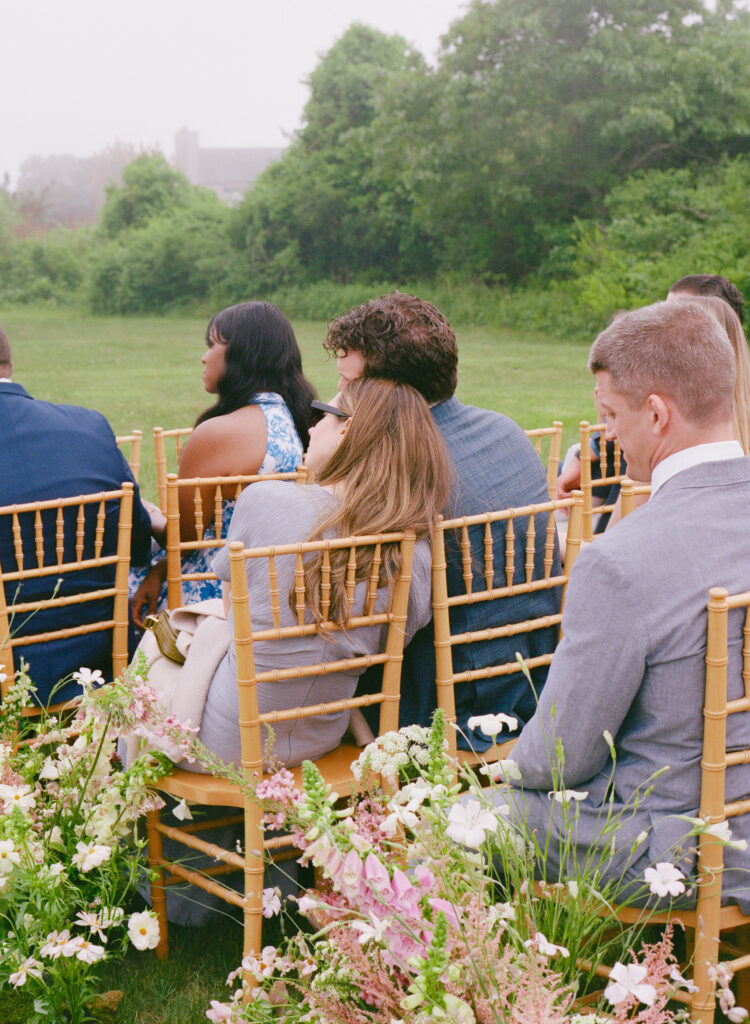 Guests seated at outdoor wedding ceremony with gold chairs and garden flowers – film wedding photography in Martha's Vineyard.