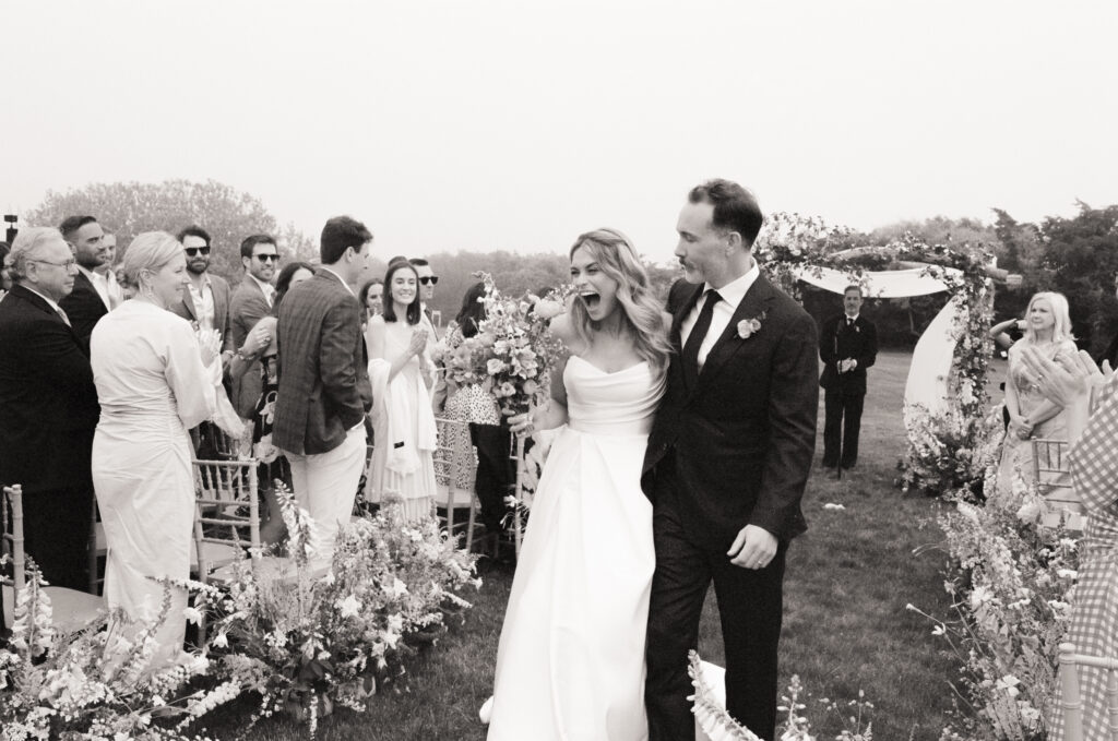 Newly married couple walks up the aisle, laughing and celebrating as guests cheer around them.