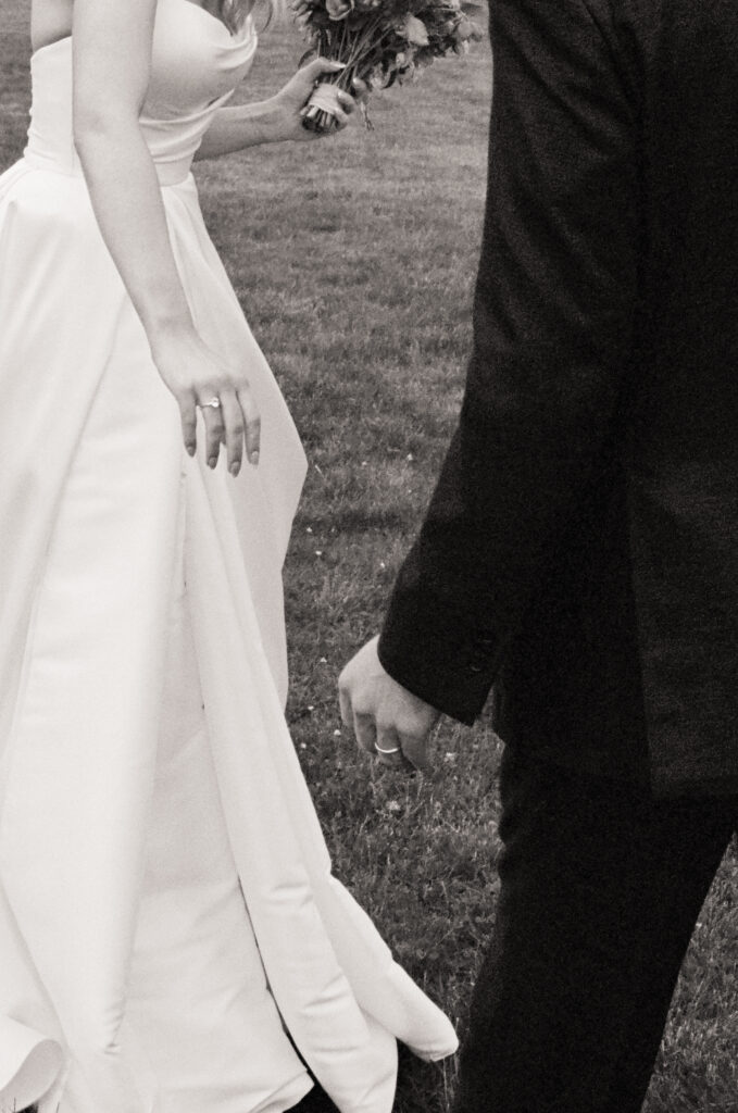 Close-up black and white image of the couple’s hands as they walk together, bride’s wedding ring visible.