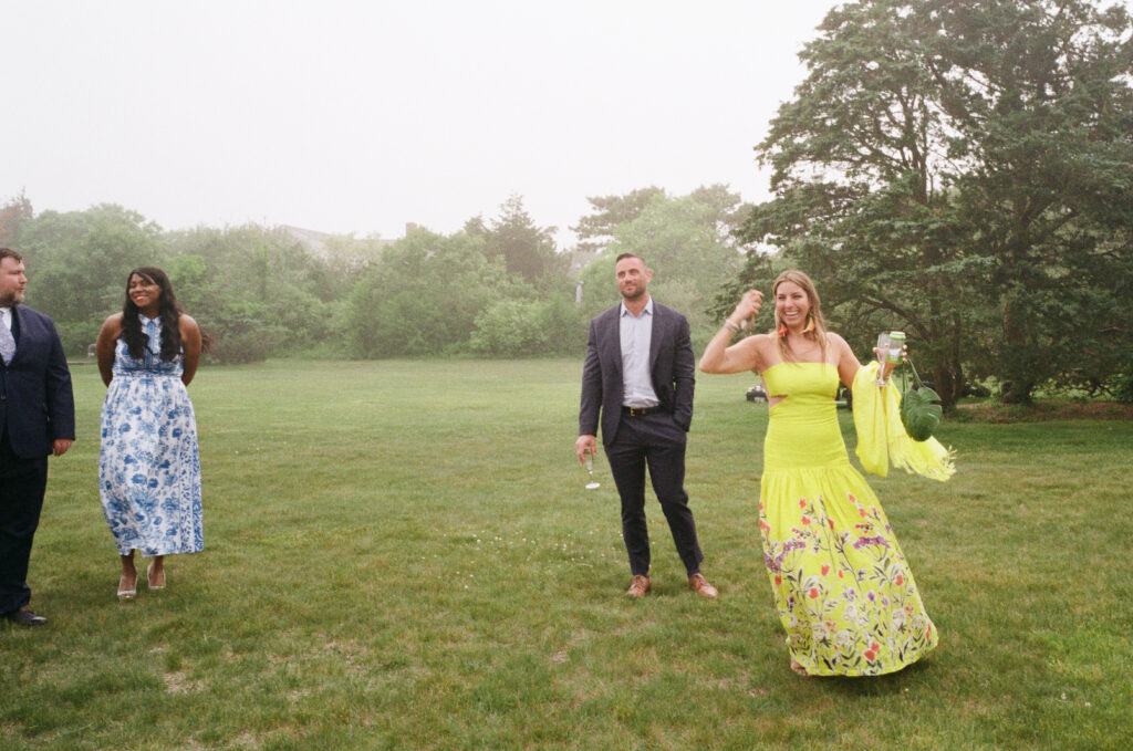 Wedding guest in a bright yellow floral dress walking across lawn at New England wedding, photographed on film