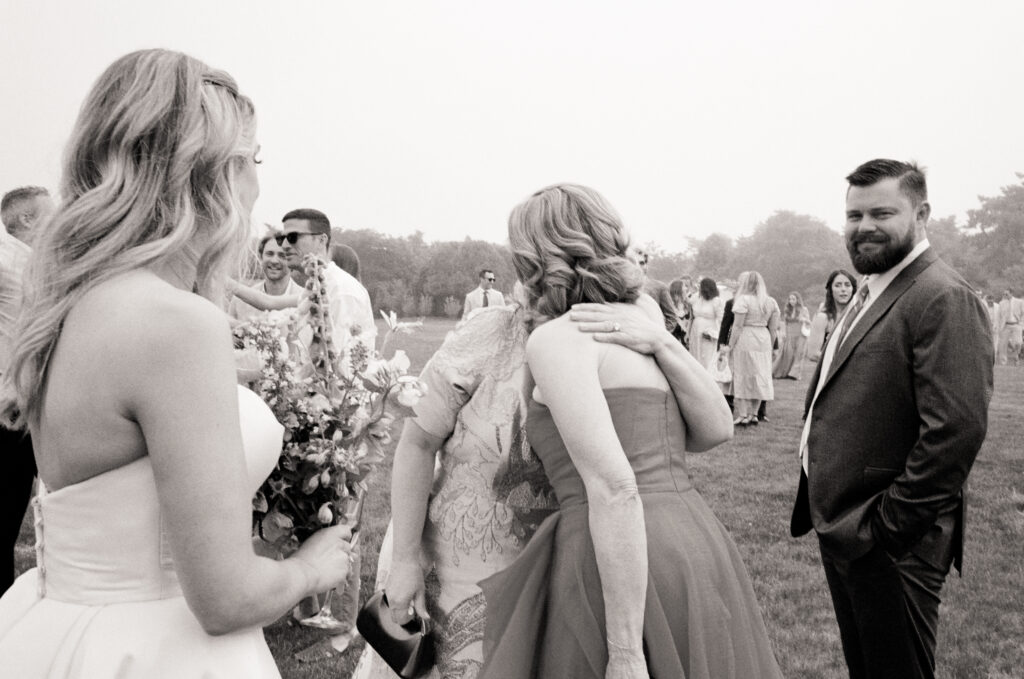 Mother of Bride in strapless gown hugging a guest in red dress while another guest smiles, candid Boston film wedding photo