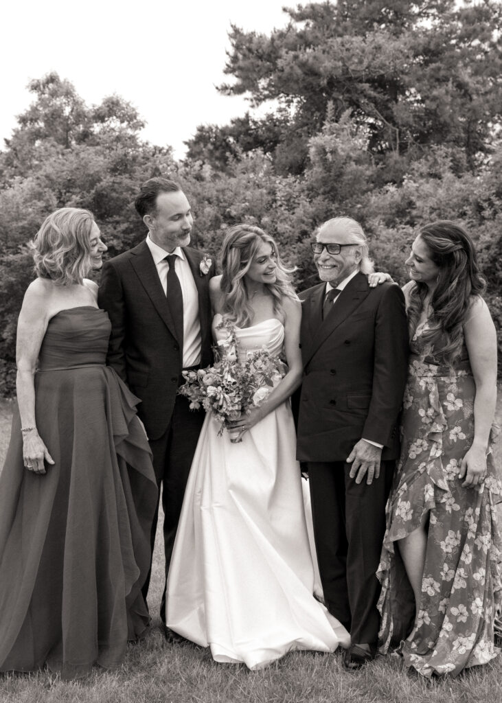 Bride and groom with family laughing together in group portrait, timeless black and white film wedding photo
