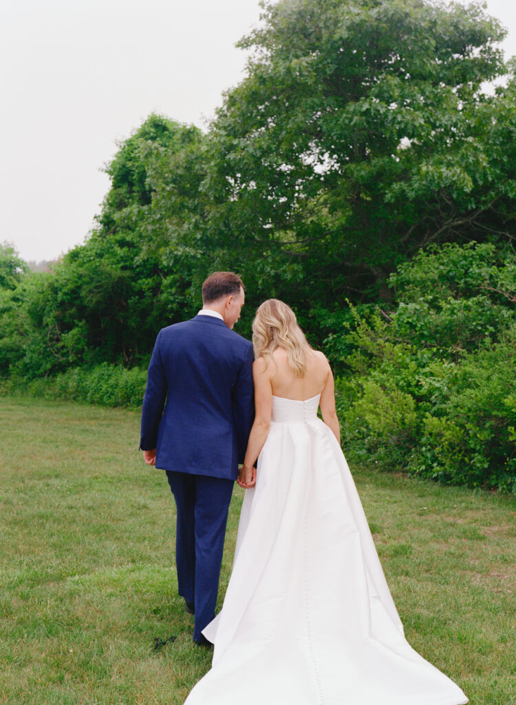 Medium format Contax 645 color film photo of bride and groom walking hand in hand through a foggy tree-lined field on Martha’s Vineyard, bride leaning her head toward the groom’s shoulder in an intimate wedding moment.