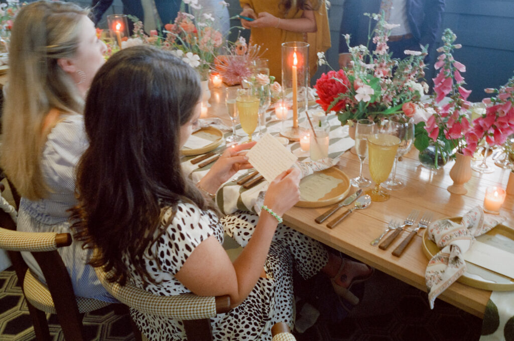Wedding guest reading a handwritten note at a dinner table decorated with flowers and candles in Martha’s Vineyard.