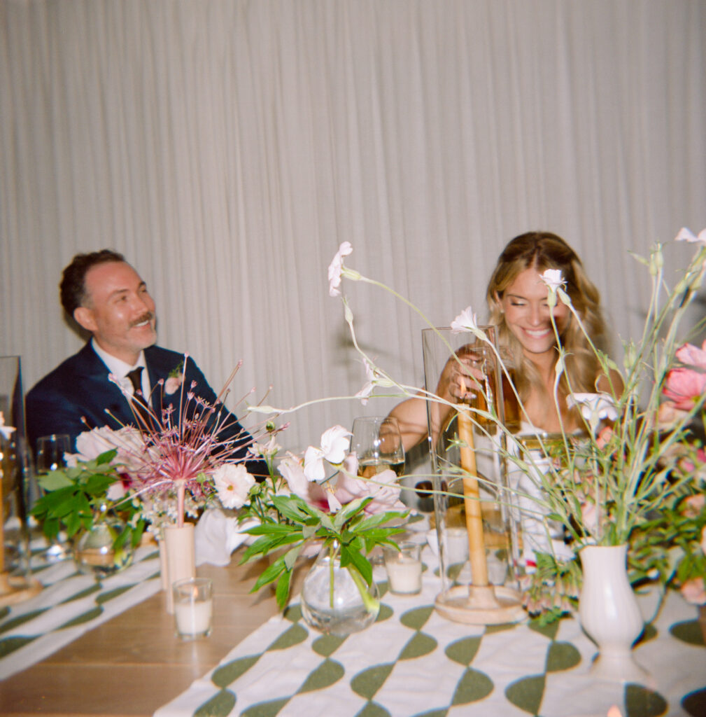 Bride and groom smiling at the head table surrounded by lush flowers during their Martha’s Vineyard wedding.