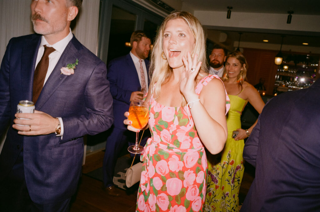 Color 35mm film flash photo of the groom’s sister-in-law in a pink floral dress cheering and cupping her hand to her mouth during the Martha’s Vineyard wedding reception dance floor.