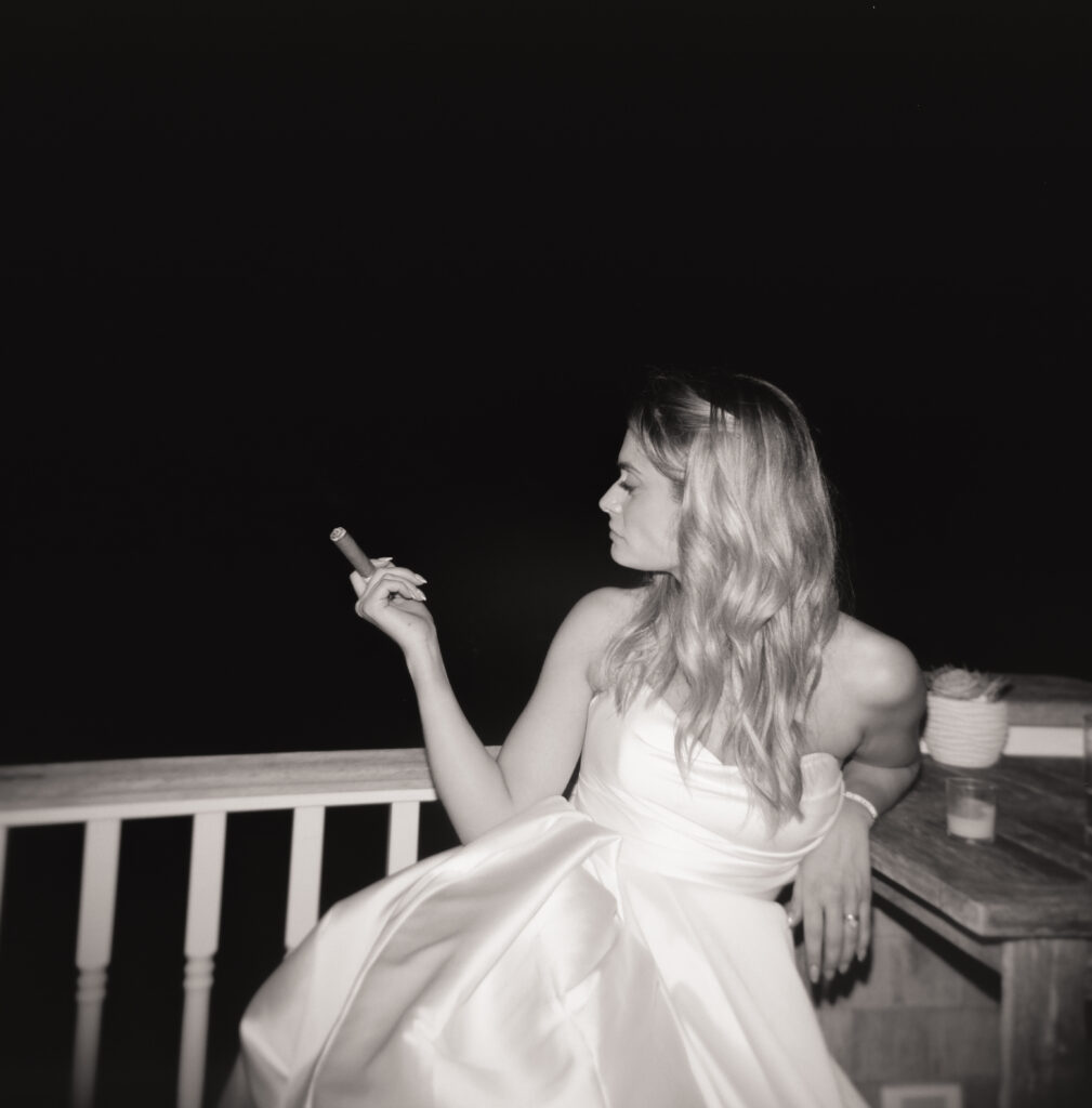 black and white film photo of the bride in her wedding dress enjoying a cigar outdoors at night.