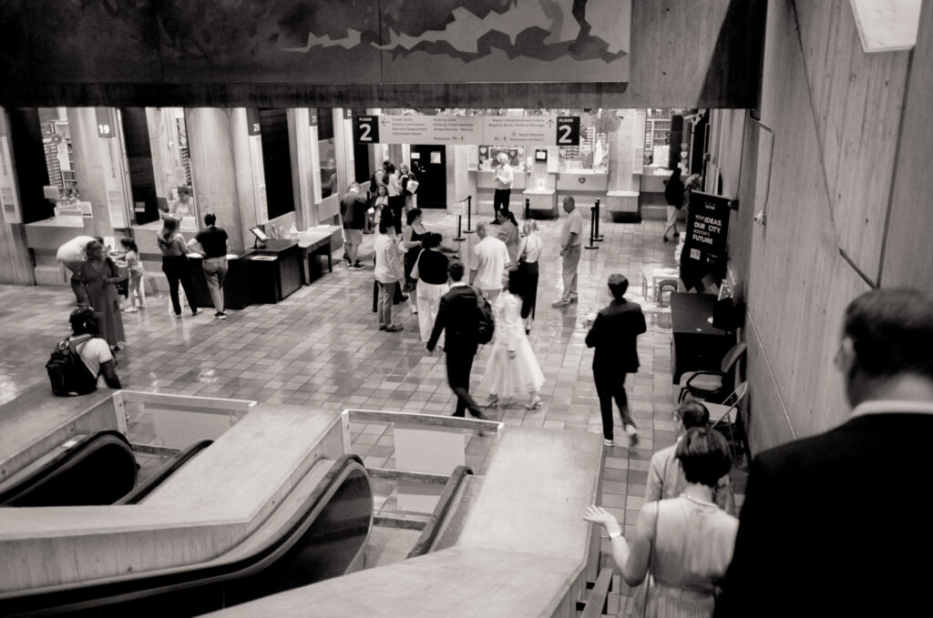 Black and white film photo wide-angle view of bride and groom among the crowd at their Boston City Hall elopement.