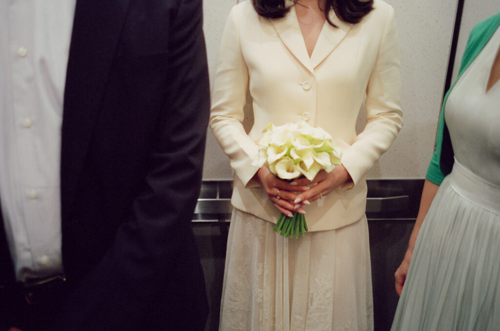 The bride holds onto her white floral bouquet in the elevator with the groom and family before their ceremony.